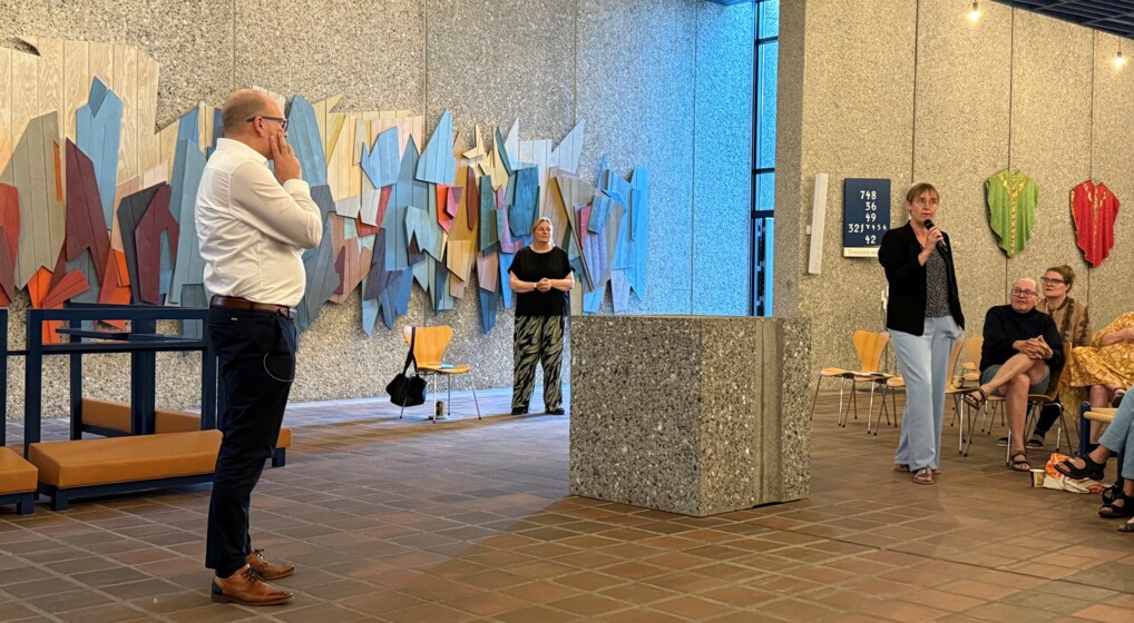 Biskop og kontorchef lytter til kvinde med mikrofon